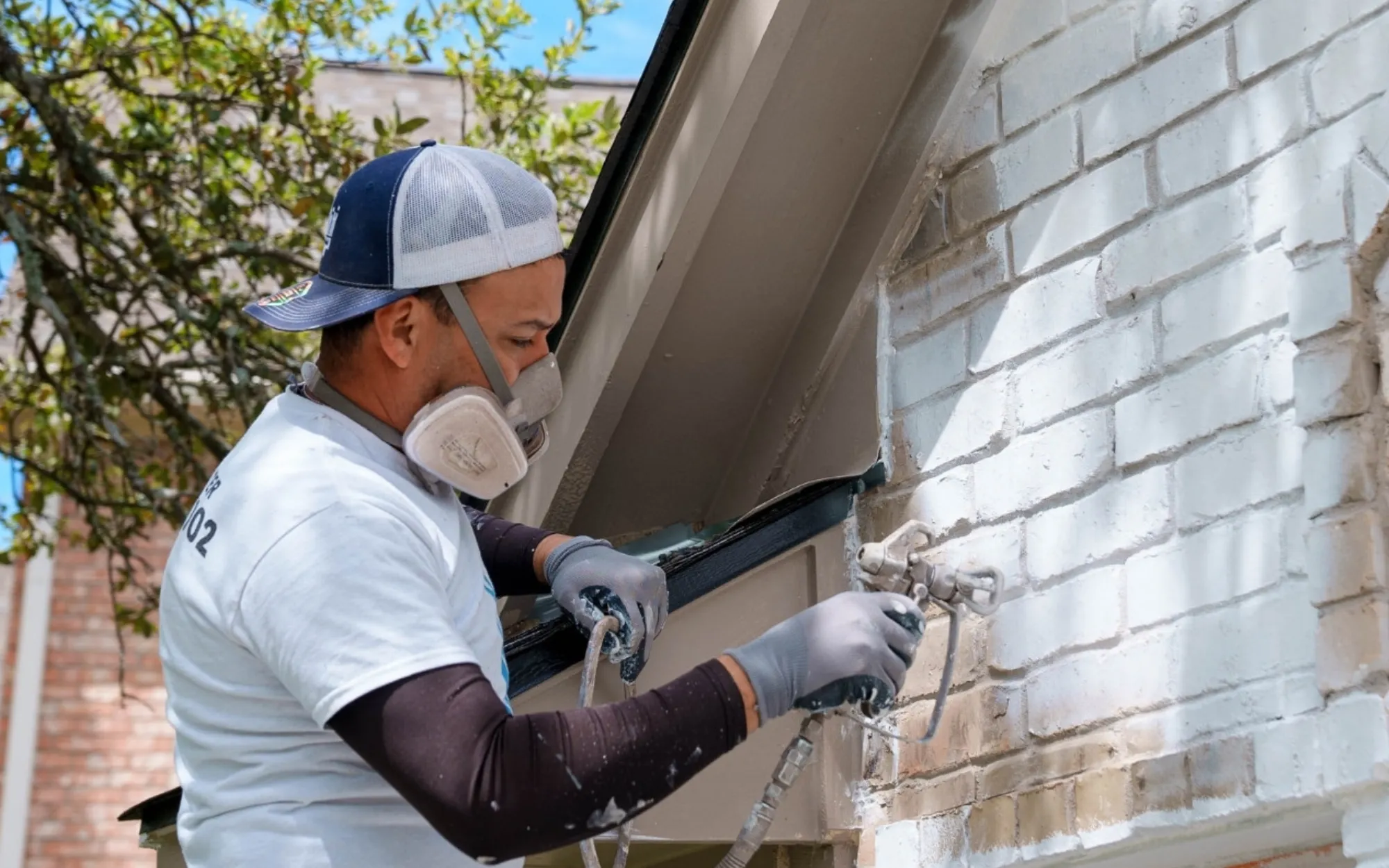 Professional painter applying breathable masonry coating to brick exterior after power washing