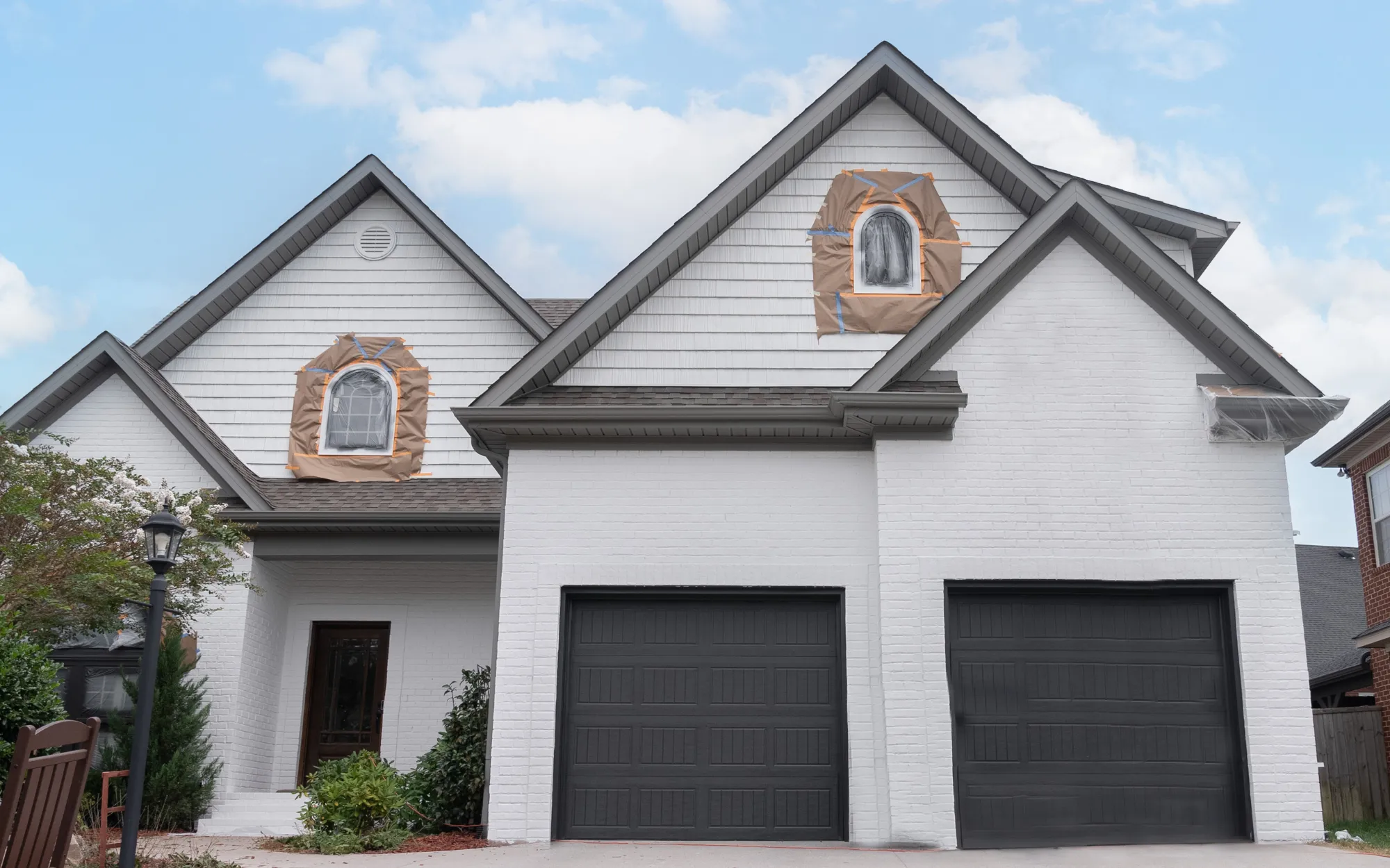 Limewashed brick home with garage and prepped windows mid-project