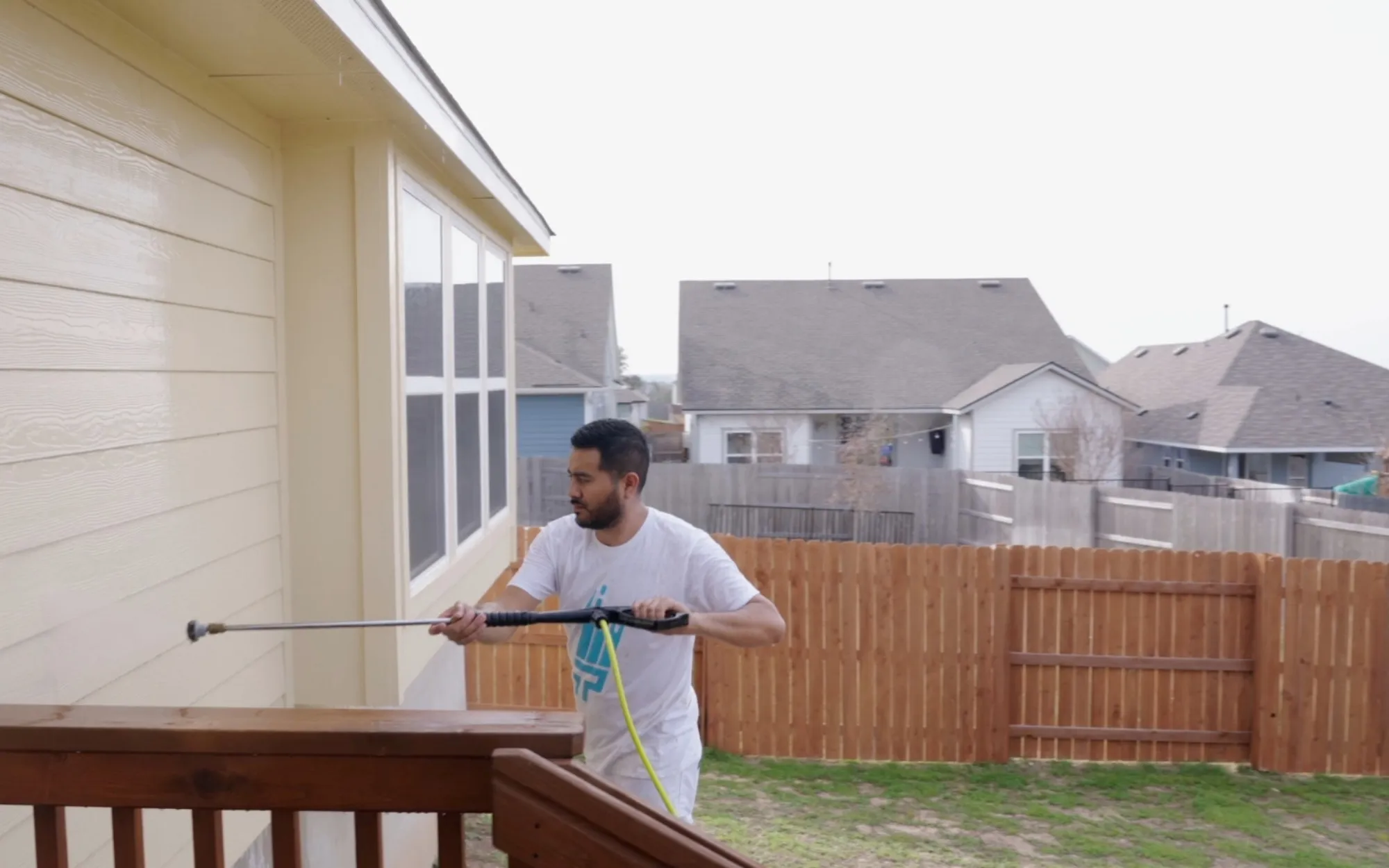 Painter pressure washing siding from a deck