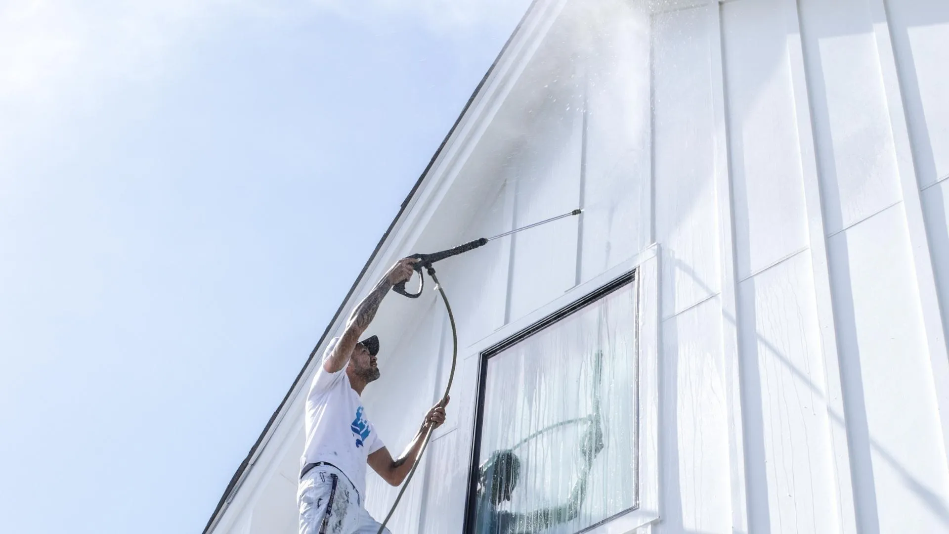 Painter pressure washing high white siding gable