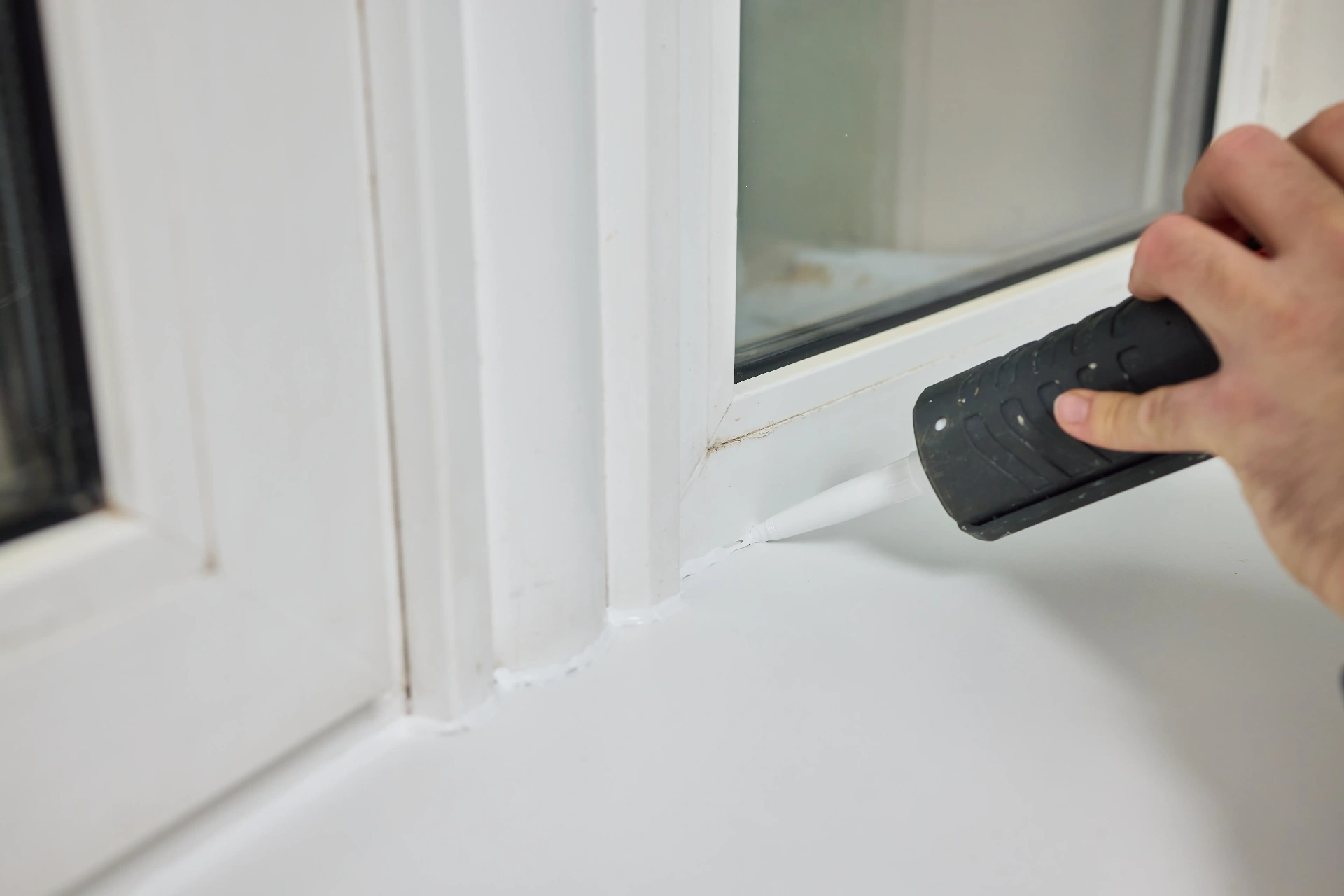 Painter applying fresh caulk along an interior window frame and sill