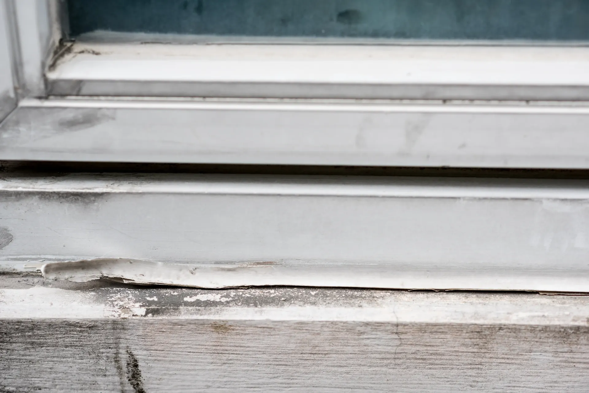 Damaged exterior window seal with peeling paint and weathered wood