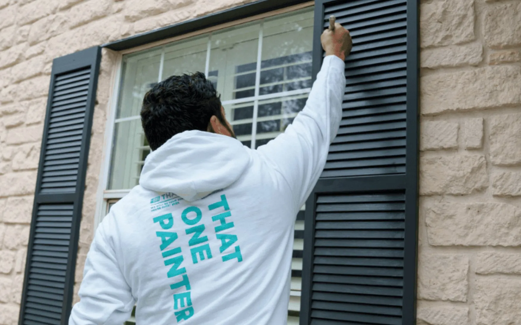 Painter refreshing exterior shutters on a stone-front home before listing