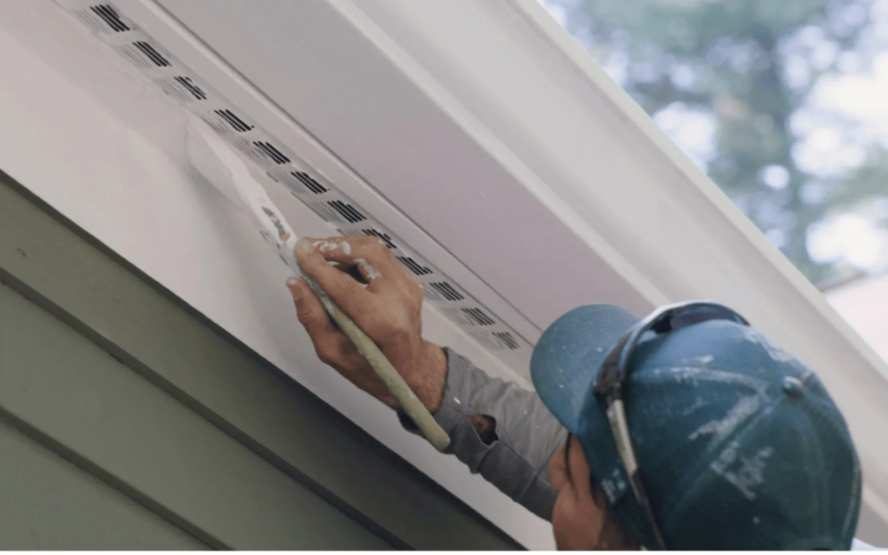 Painter sealing exterior soffit and trim lines as part of sale-prep work